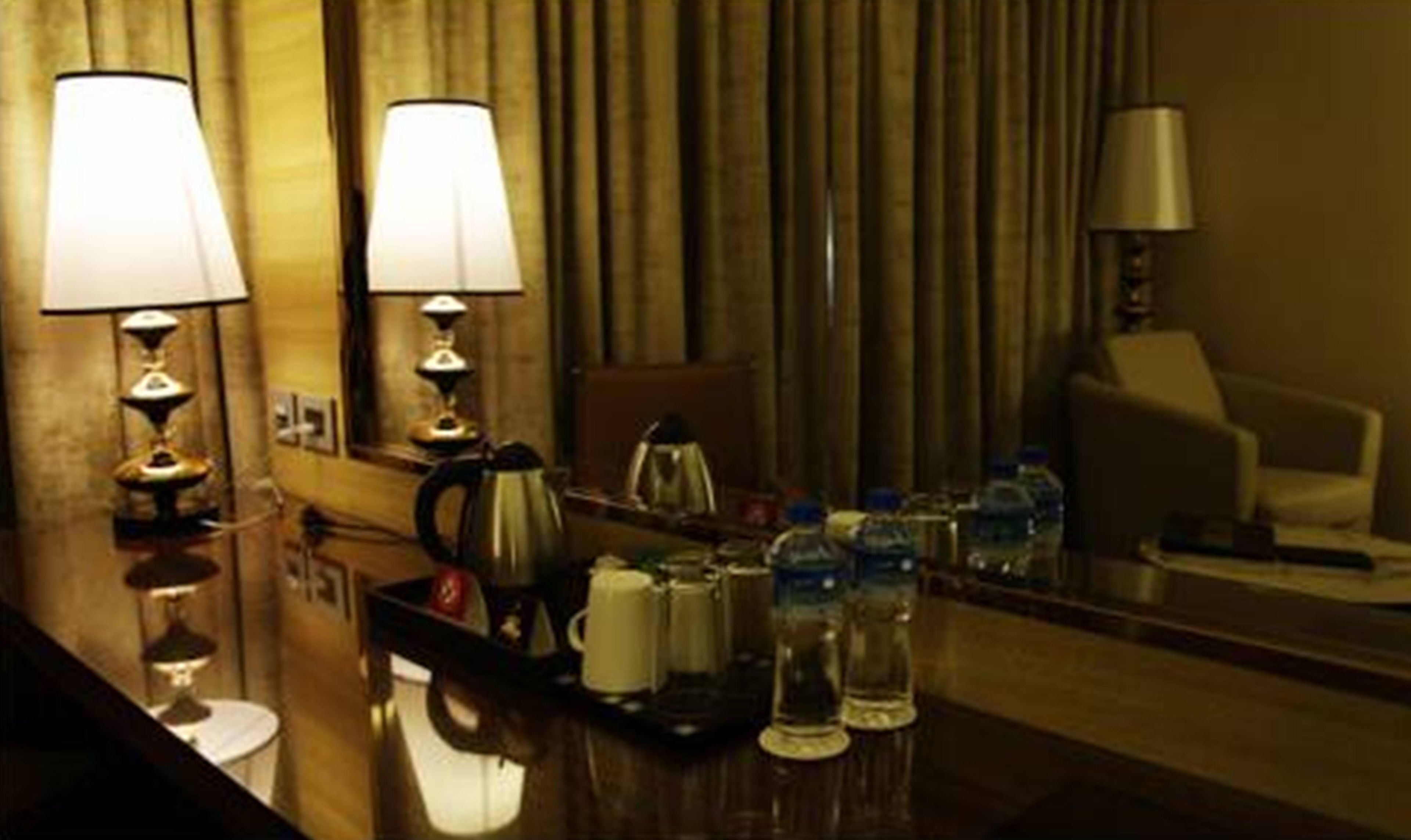 A hotel room with a wooden desk, two lamps, a mirror, a chair, and a coffee maker.