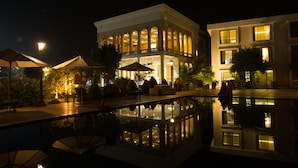 A nighttime view of a hotel with a pool, outdoor seating, and well-lit windows. - UVA Meridian bay resort and spa (Kundapur)