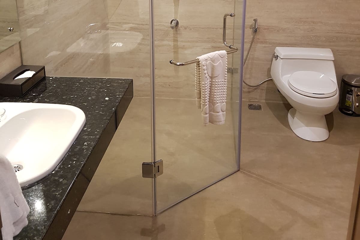 Et moderne badeværelse med en glasvægs brusekabine, et hvidt toilet og en sort bordplade med vask.