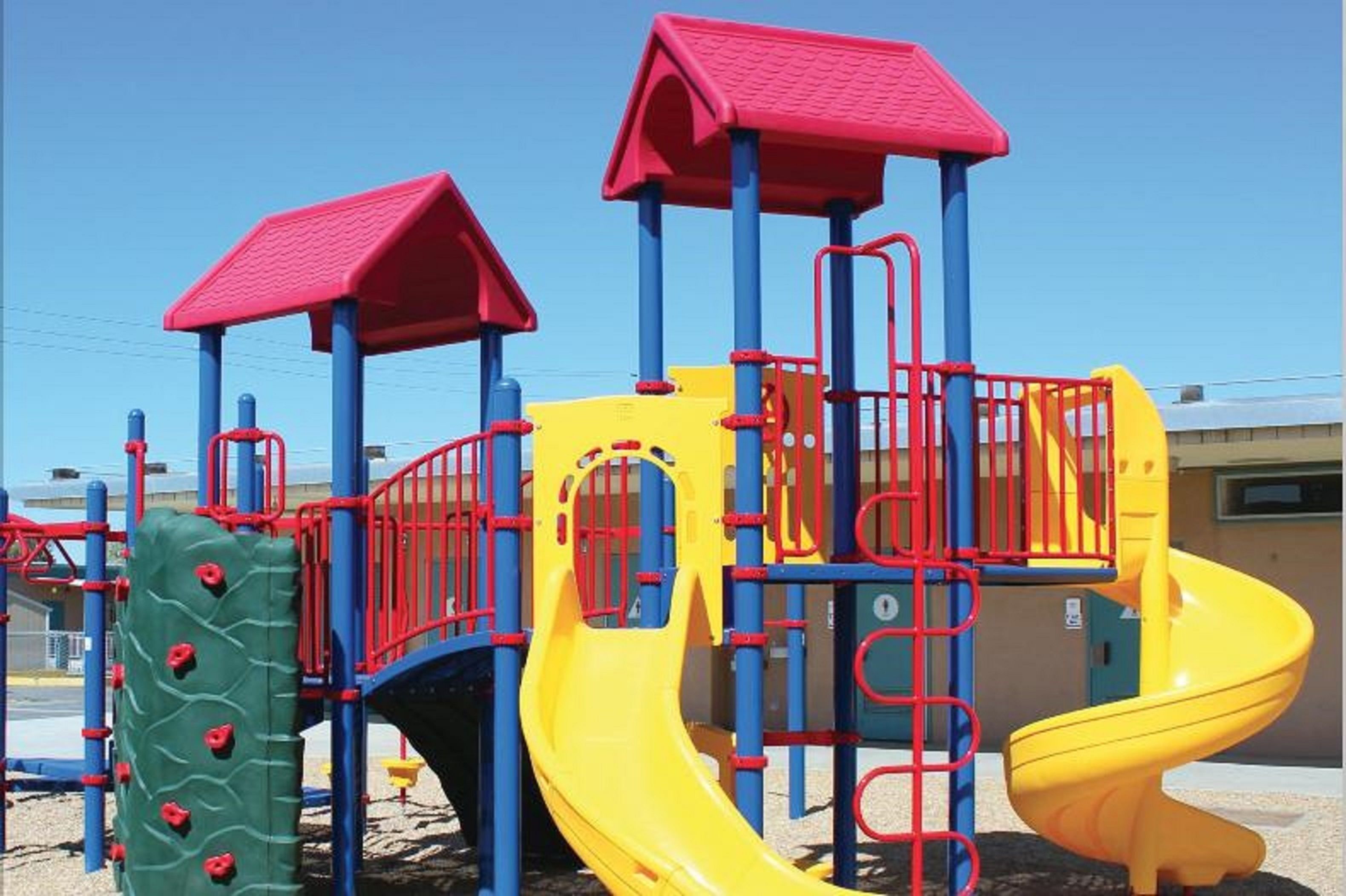 A playground with a yellow slide, red and blue climbing structures, and a green climbing wall.