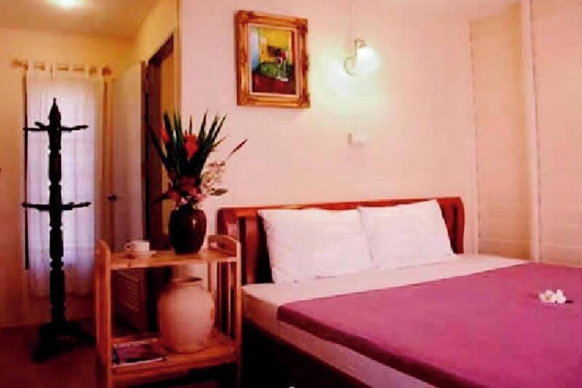 A hotel room with a bed, a nightstand, a wall-mounted light, and a framed picture.