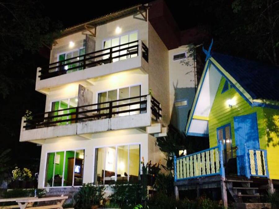 Un edificio de dos pisos con balcones y una casa cercana de colores brillantes.