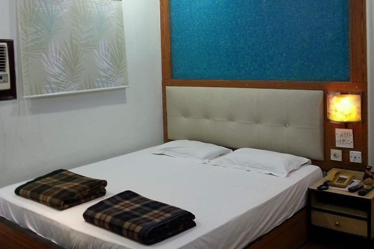 Una habitación de hotel con una cama grande, un cabecero con panel azul, una mesita de noche con lámpara y una ventana con diseño de hojas.