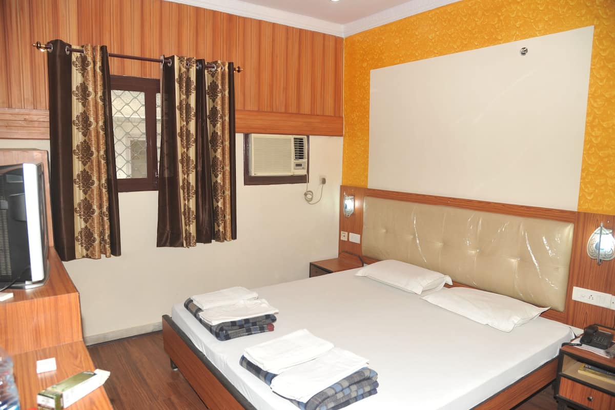 Habitación de hotel con cabecera de madera, cama con ropa blanca, mesita de noche con lámpara y ventana con cortinas.