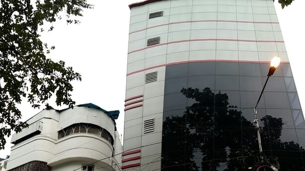 Un hotel con fachada moderna, que incluye un amplio ventanal reflectante y un letrero que dice "Hotel Akash Ganga".