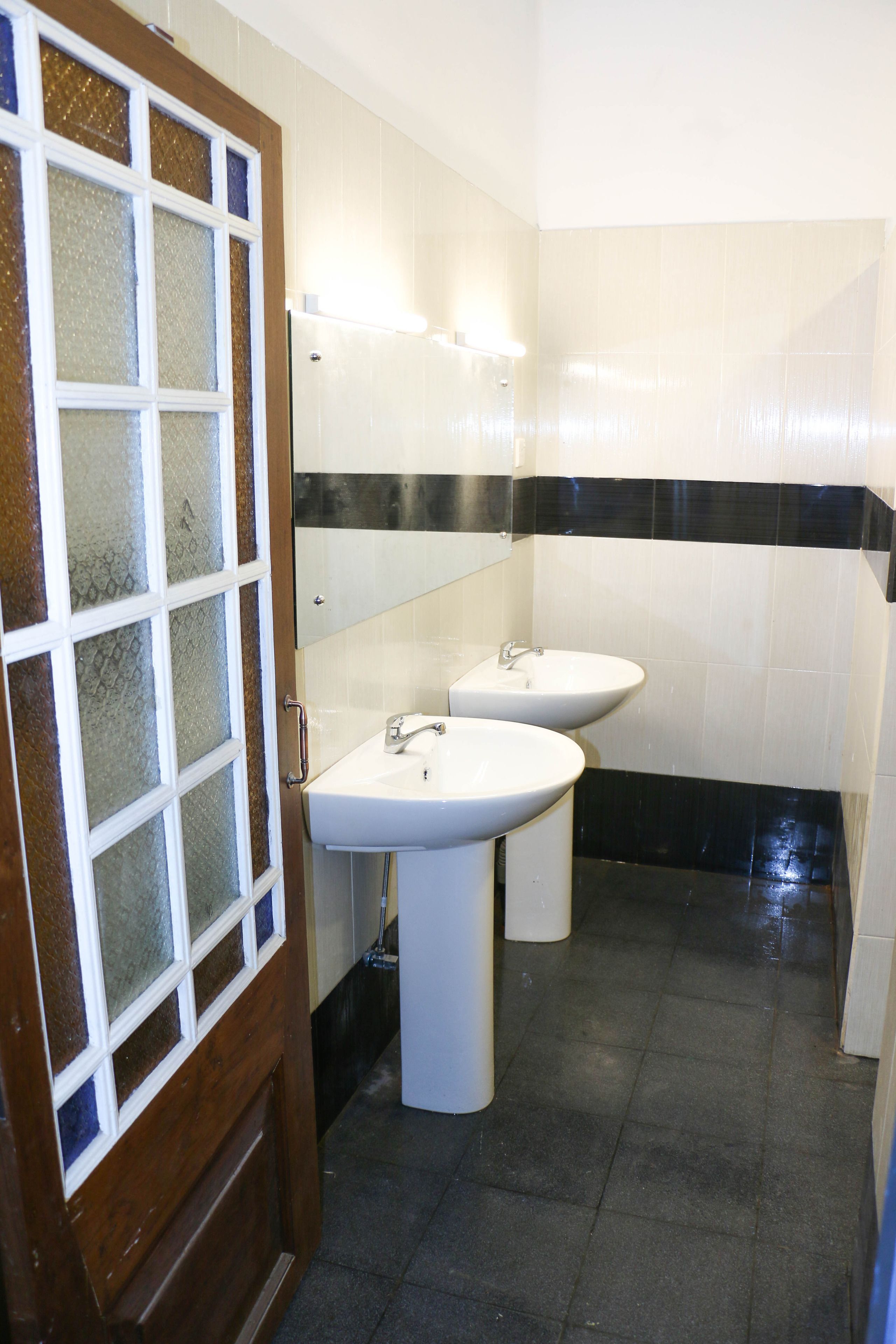 Ein Badezimmer mit zwei Waschbecken, einem Spiegel und einer Tür mit satinierten Glaselementen.