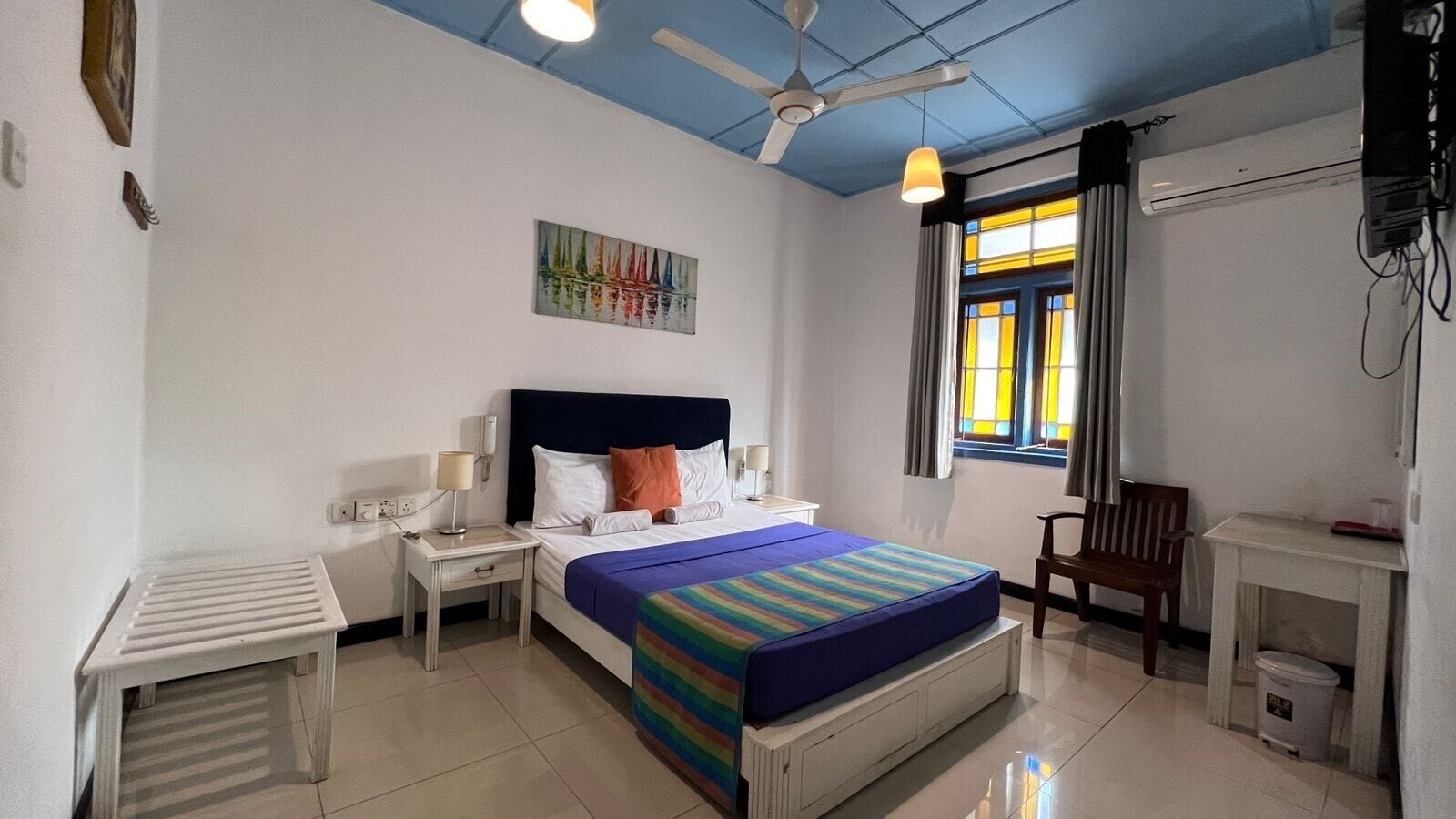 A hotel room with a bed, bedside table, lamp, and a window with curtains.