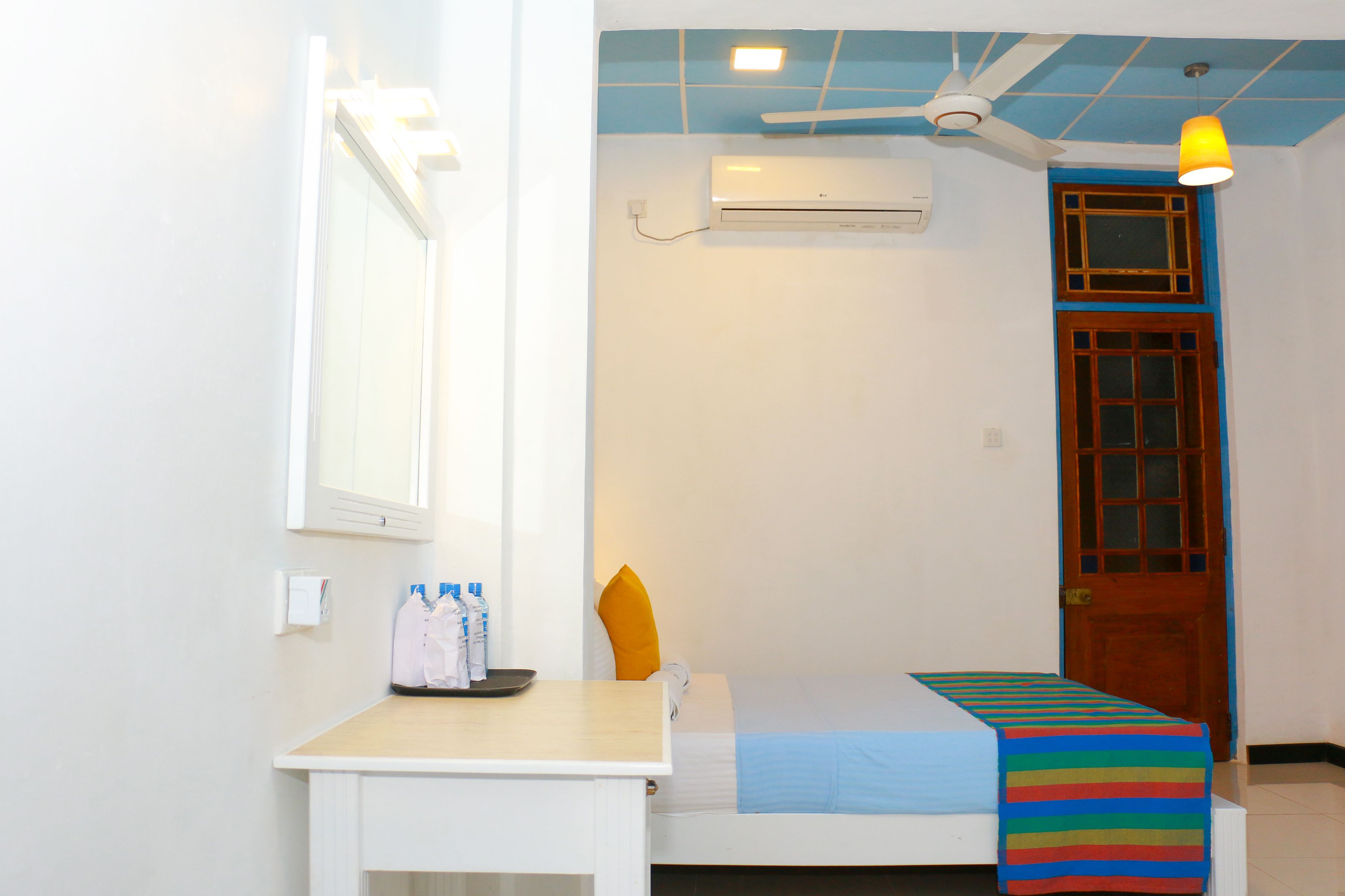 A small, clean room with a bed, a desk, a window, and an air conditioning unit.