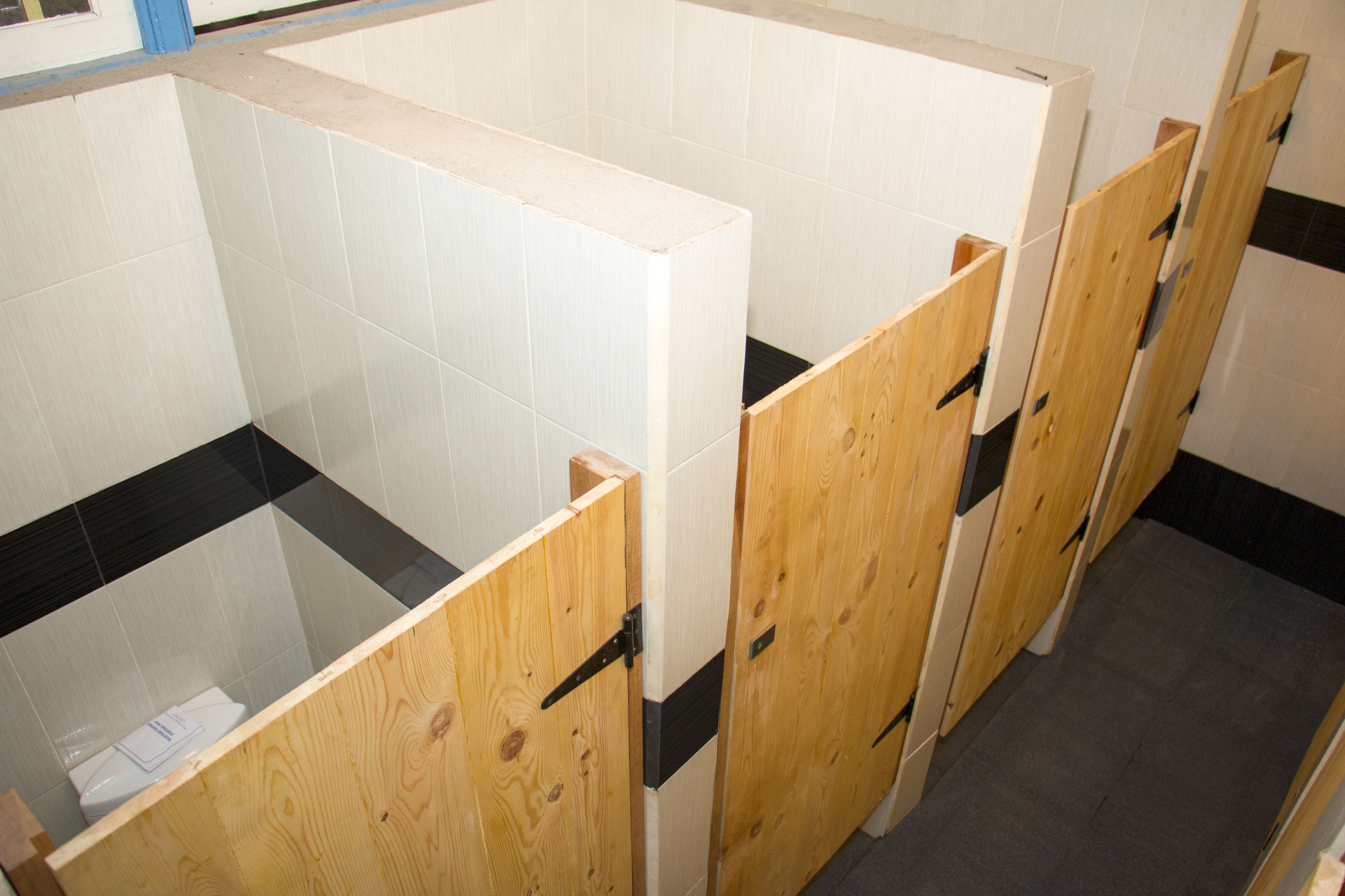 A row of wooden partitioned bathroom stalls with white tiled walls and a black and white striped floor.