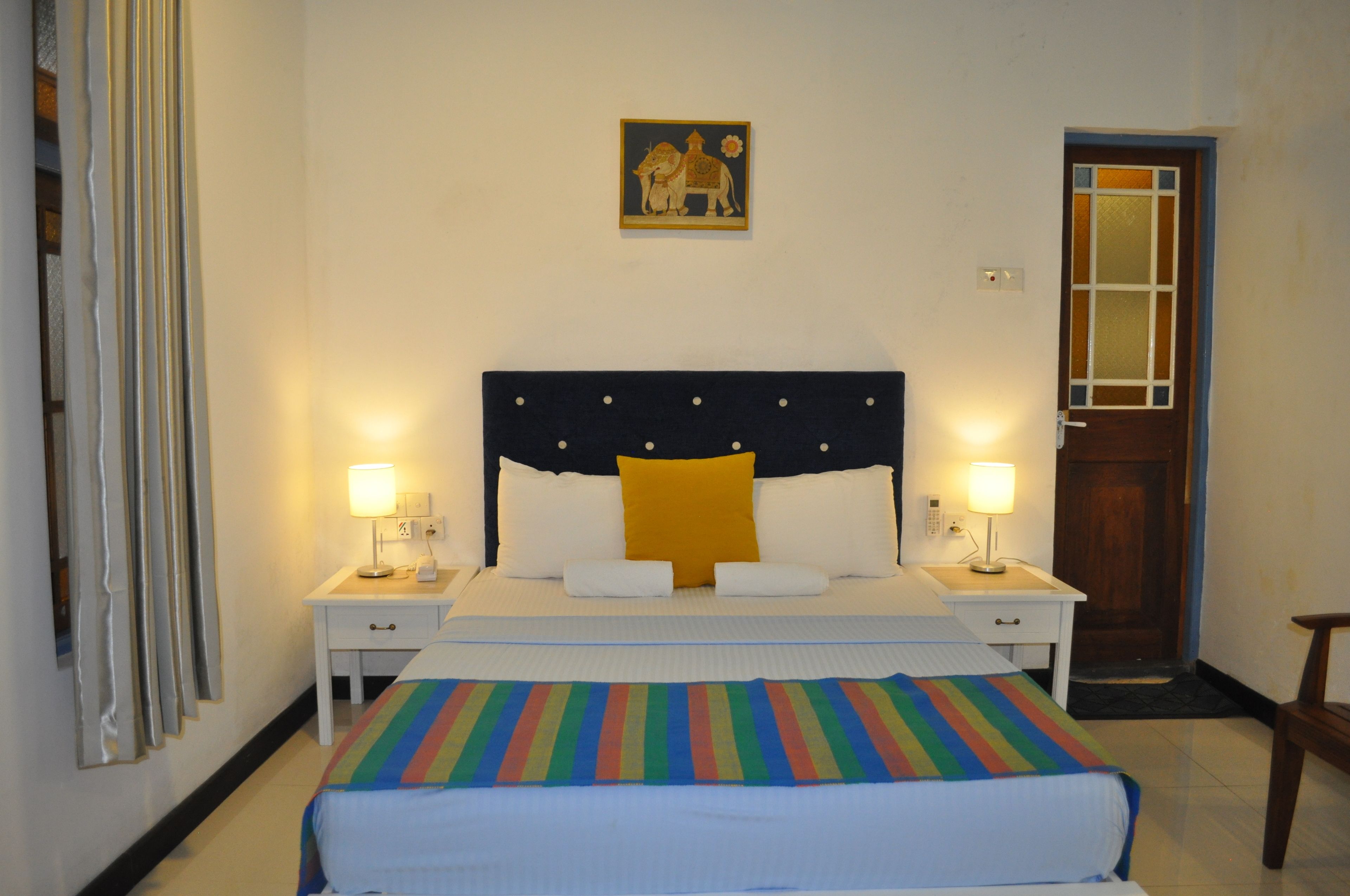 A hotel room with a bed, two bedside tables, a nightstand, a door, and a wall-mounted picture.
