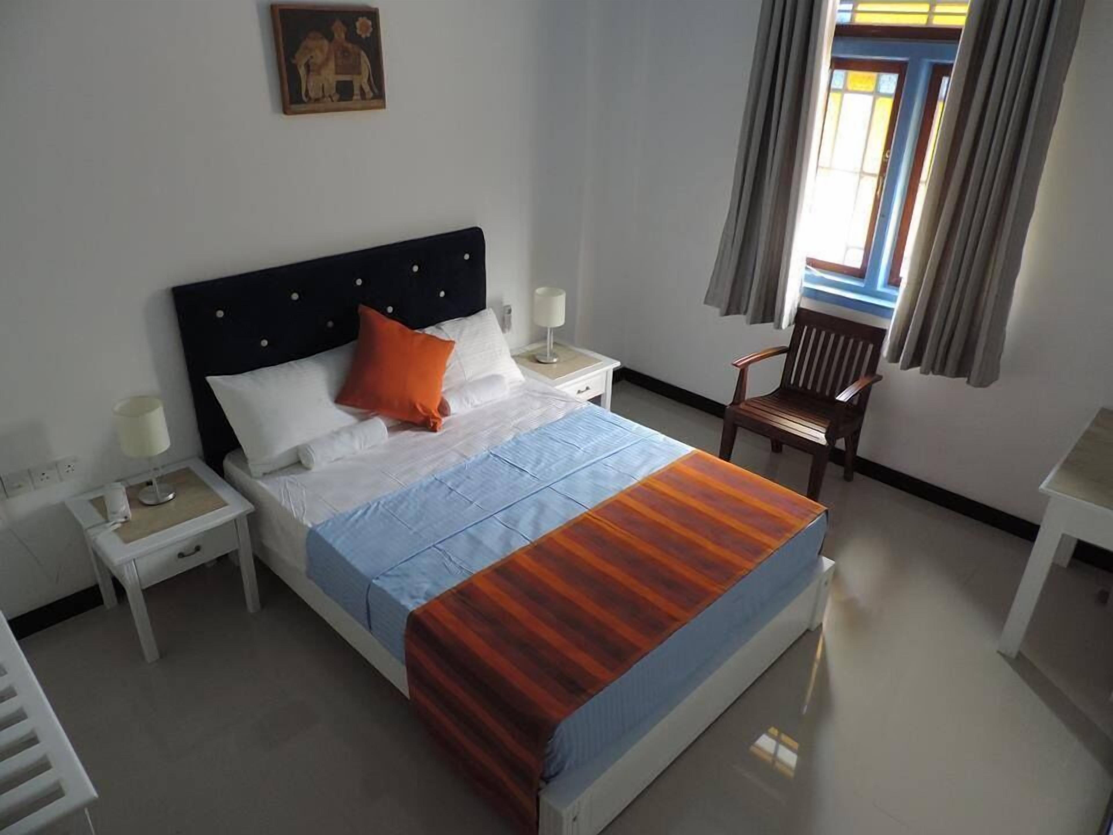 Cama bem arrumada com manta listrada, mesa de cabeceira com abajur, uma cadeira e um quadro na parede.