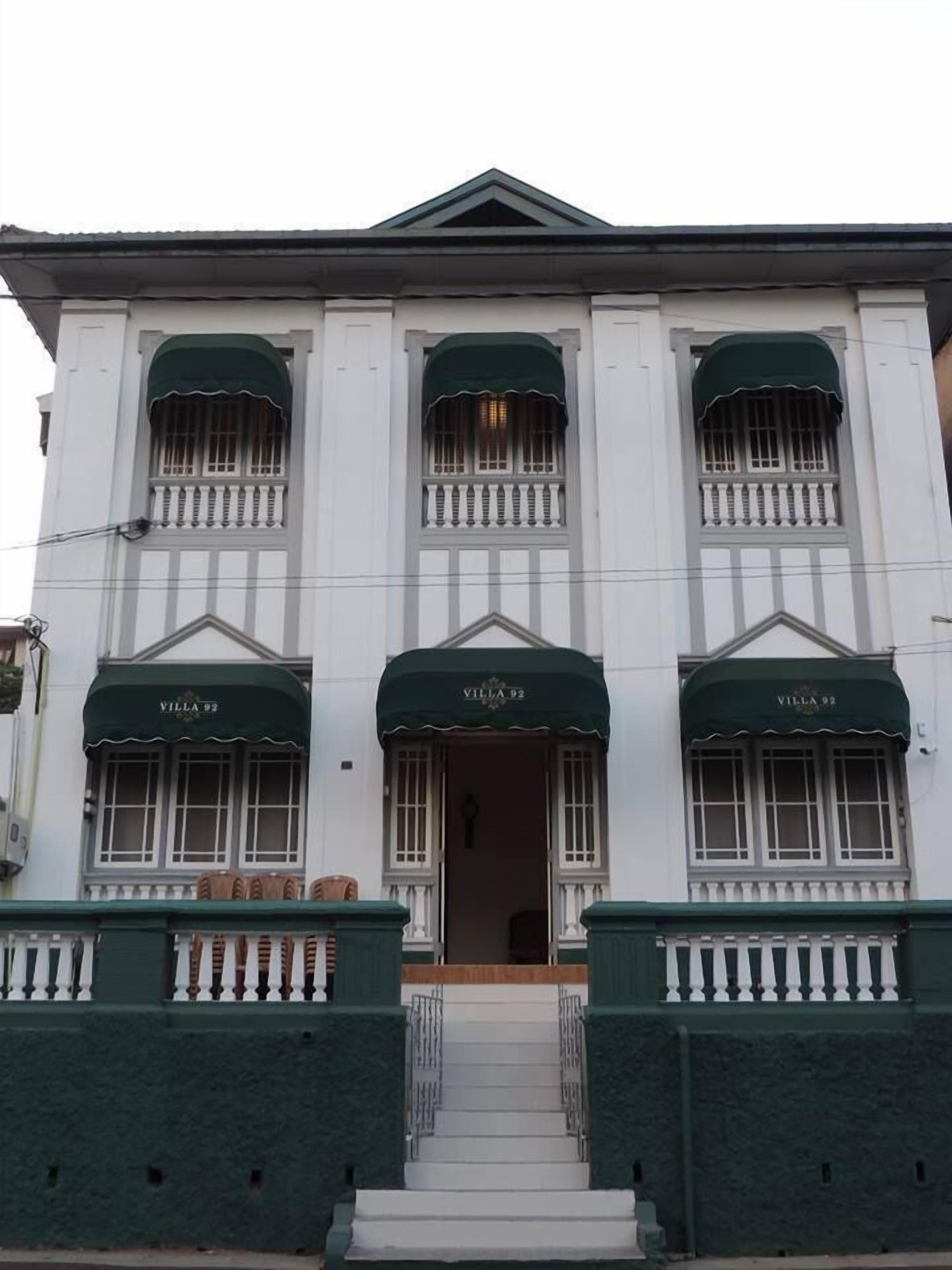 A building with three arched windows, each with a green awning labeled "Villa 92".