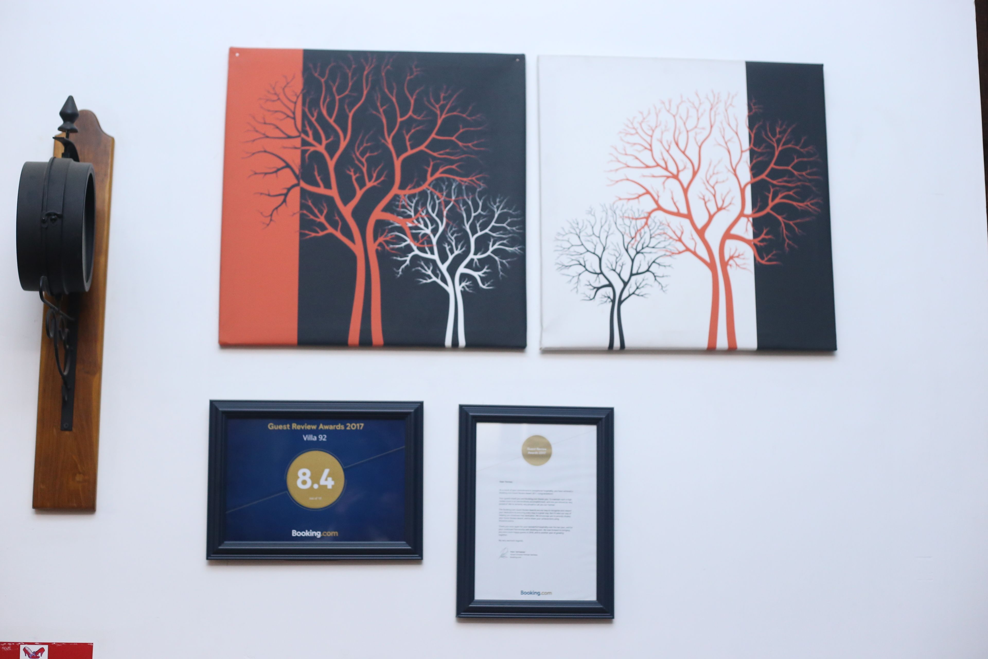 Dos obras de arte enmarcadas que muestran árboles estilizados, un premio por reseñas de huéspedes enmarcado y un certificado en la pared.