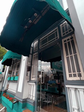 Un edificio con un toldo verde, un letrero que dice "Villa 92" y una entrada con puerta de vidrio.