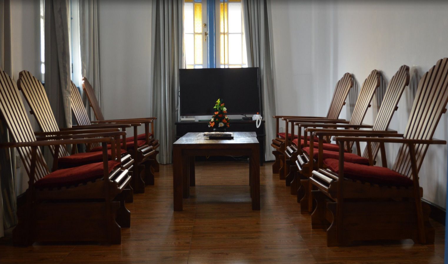 A conference room with a long table and rows of wooden chairs with red cushions.