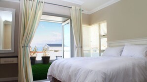 A bedroom with a large bed, a window with curtains, and a view of the outside. - Spatalla Holiday Homes (Kleinmond)