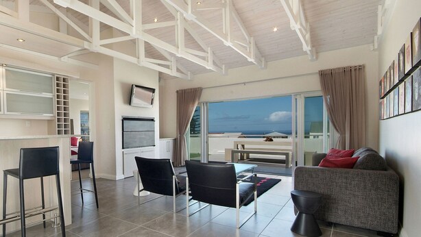 A spacious living area with a high ceiling, a balcony with a view, and a kitchen area with modern appliances. - Spatalla Holiday Homes (Kleinmond)