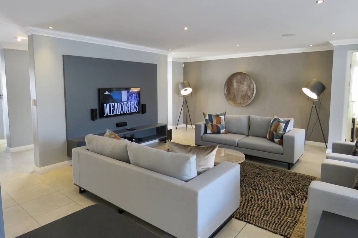 Una sala de estar moderna con un sofá gris, un televisor montado en la pared y dos lámparas de pie.