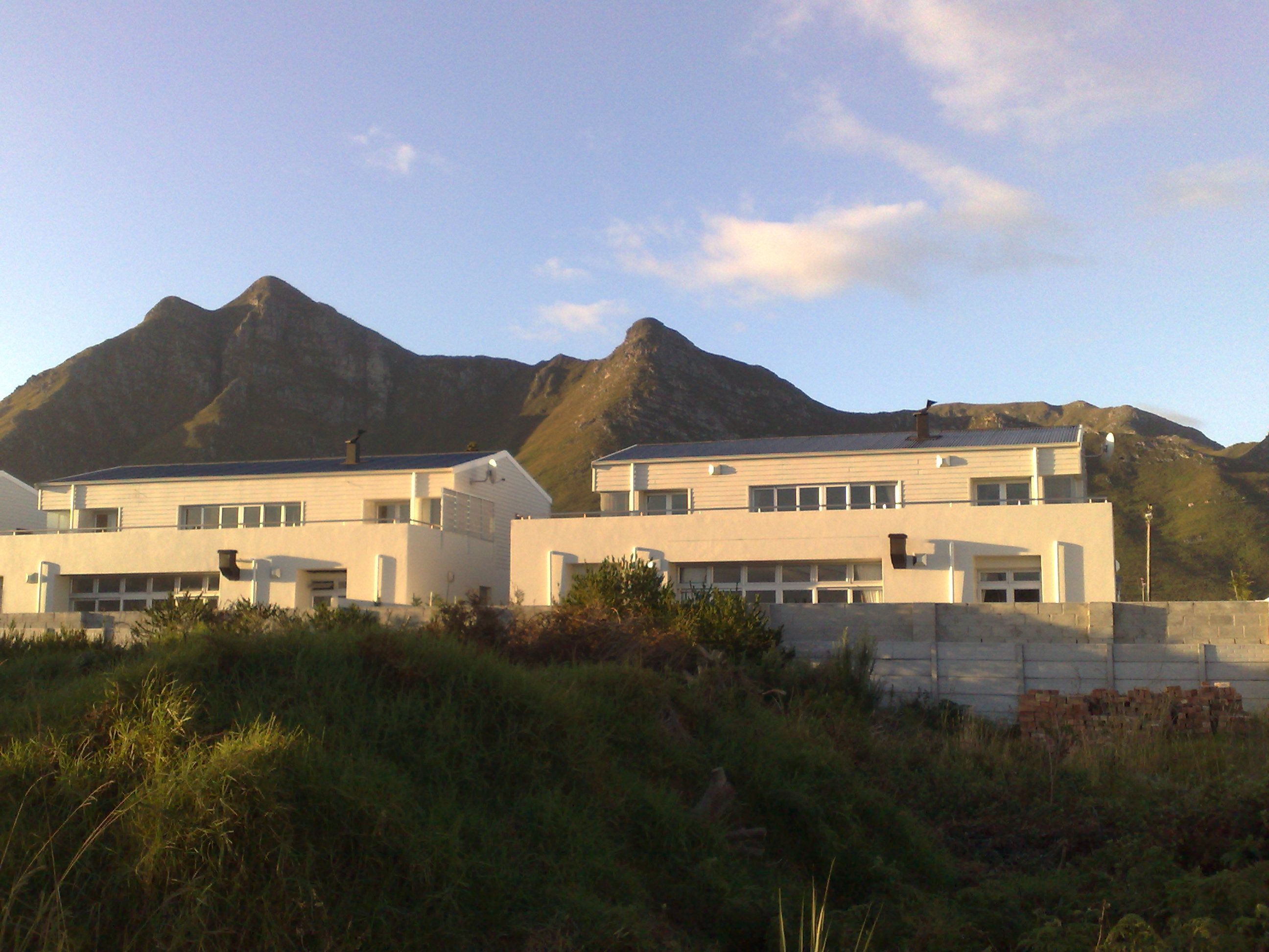 A modern building with a flat roof, multiple windows, and a garage. It is surrounded by grass and a mountain is visible in the background.