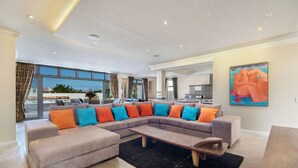 A spacious living room with a large sectional sofa, a wooden coffee table, and a painting on the wall. - Spatalla Holiday Homes (Kleinmond)