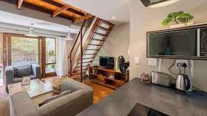 A modern living room with a staircase, a flat-screen TV, and a kitchen area with a kettle and toaster. - Raptors Lodge (Hoedspruit)
