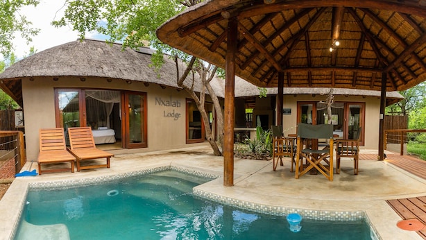 A pool area with wooden lounge chairs, a thatched-roof structure, and a building labeled "Nxalat Lodge". - Raptors Lodge (Hoedspruit)