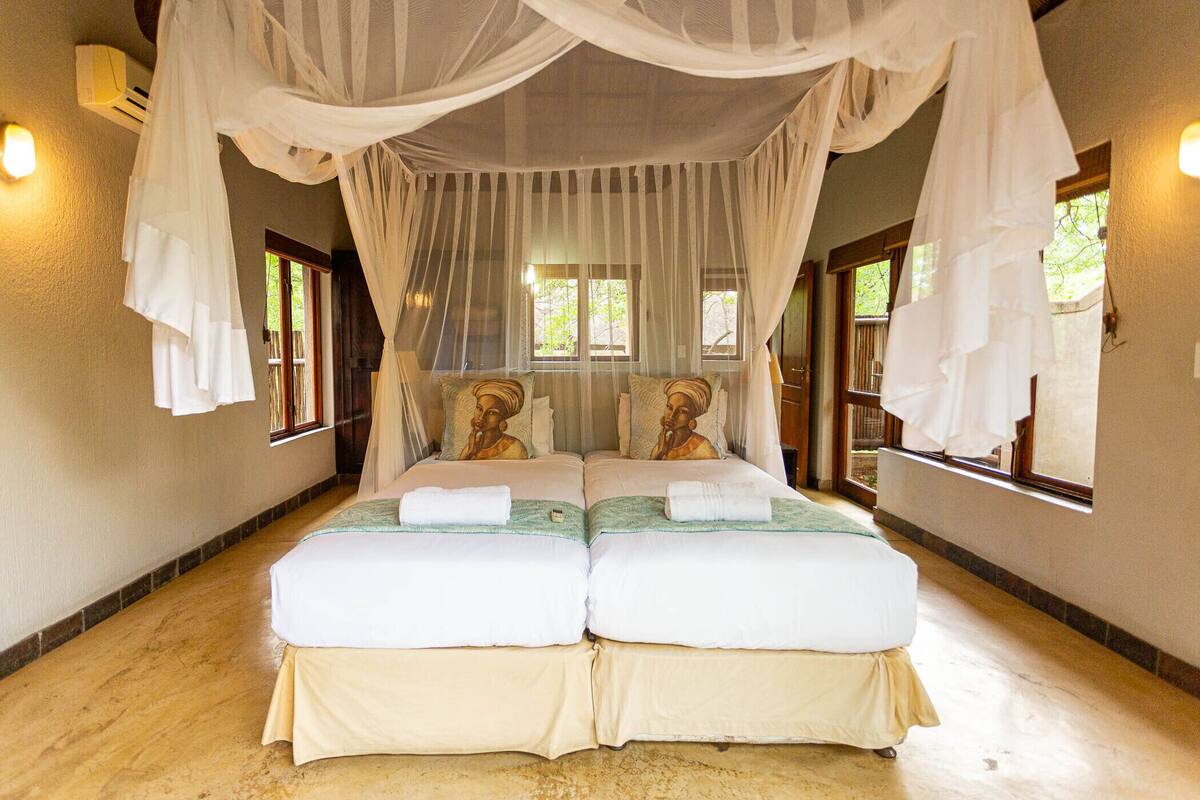 Una habitación con cama bajo un dosel, dos ventanas y suelo de madera.