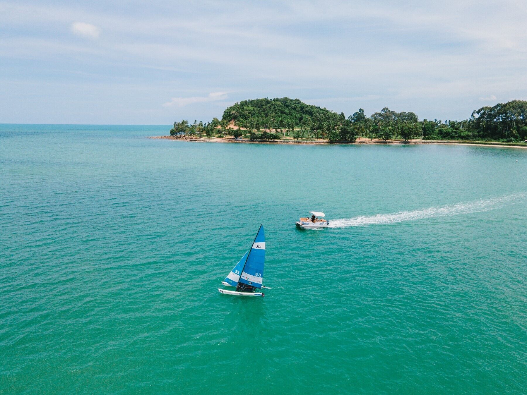 Un velero en aguas turquesas con una isla boscosa al fondo.