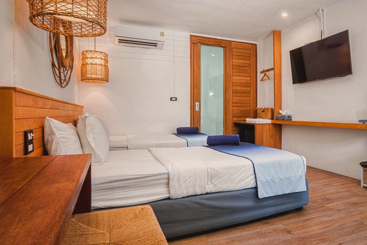 A bedroom with a bed, bedside table, hanging wicker lamps, a TV, and a wooden shelf.