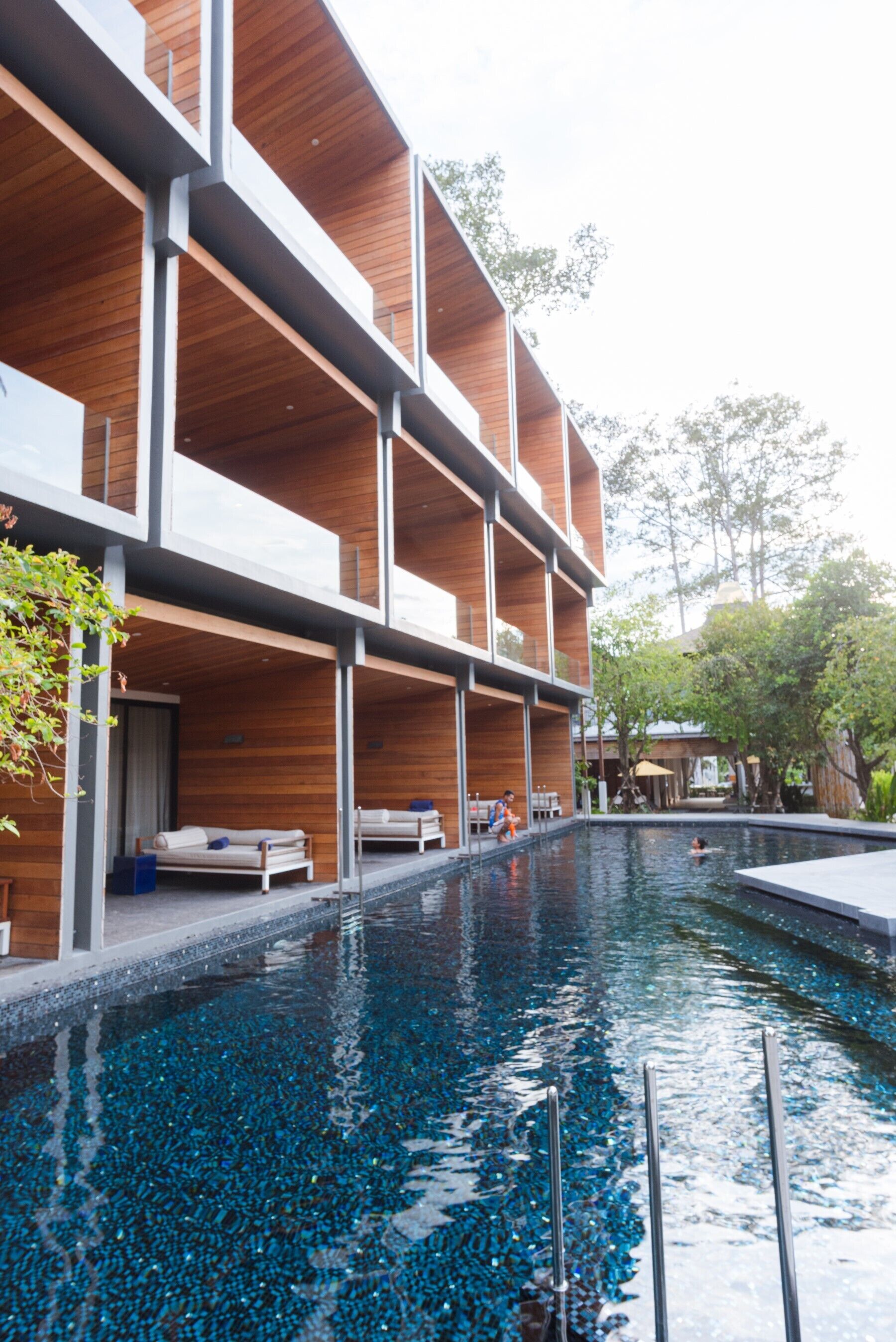 A modern building with a pool area, featuring wooden paneling and a clear blue pool.