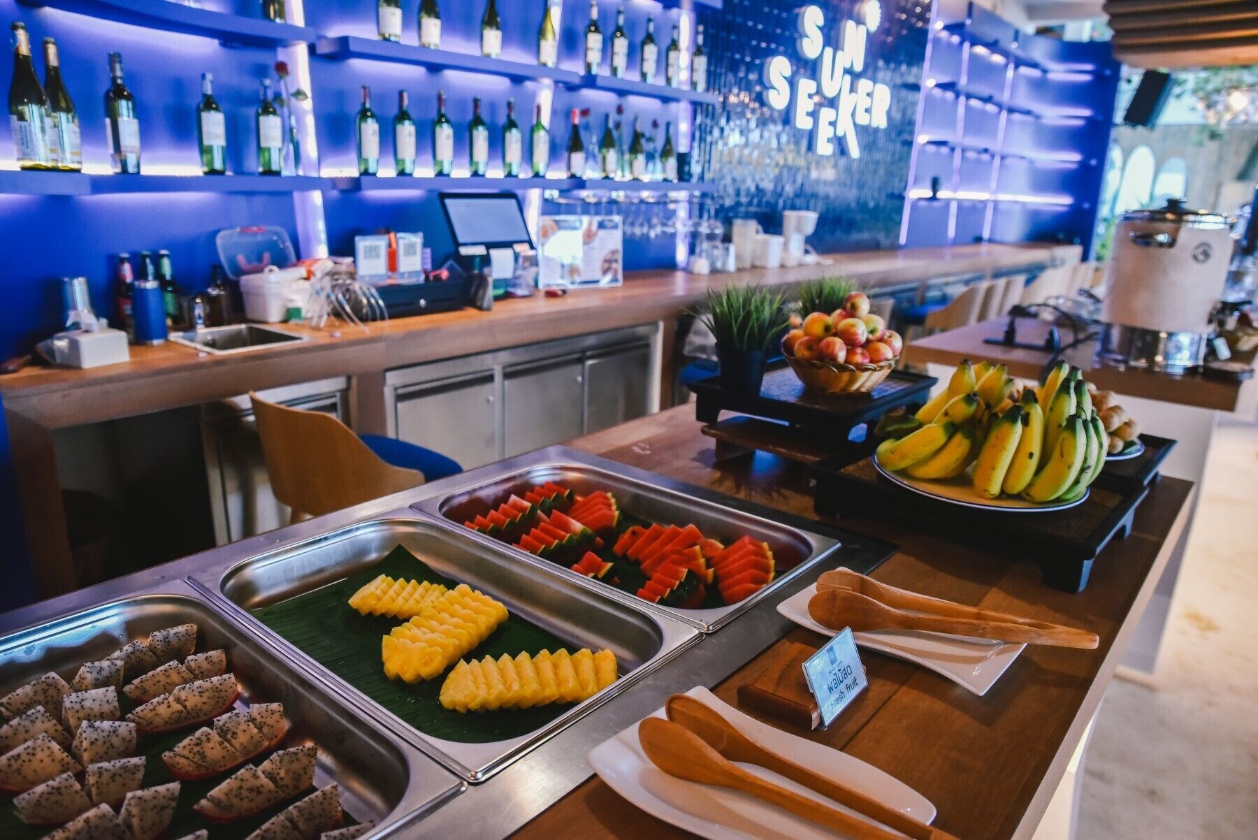 A buffet with various fruits and vegetables, a bar area with bottles, and a sign indicating 'Fresh fruit'.