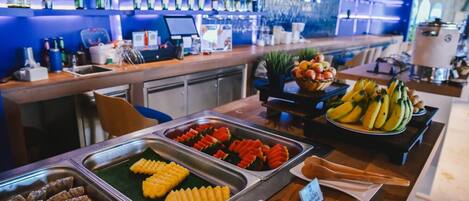 A buffet with various fruits and vegetables, a bar area with bottles, and a sign indicating 'Fresh fruit'.