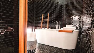 A modern bathroom with a black-tiled wall, a white bathtub, and a wooden ladder.