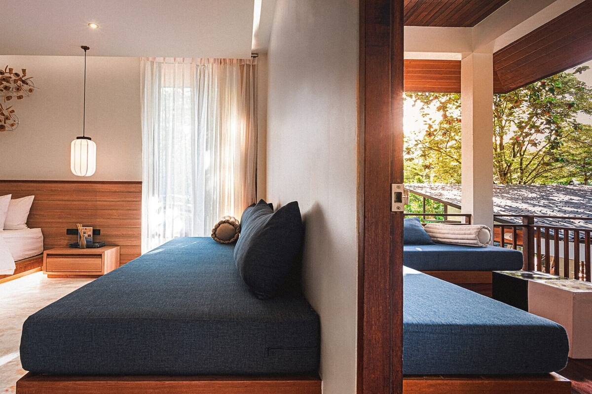 A bedroom with a large bed, a bedside table, a lamp, and a view of the outdoors.