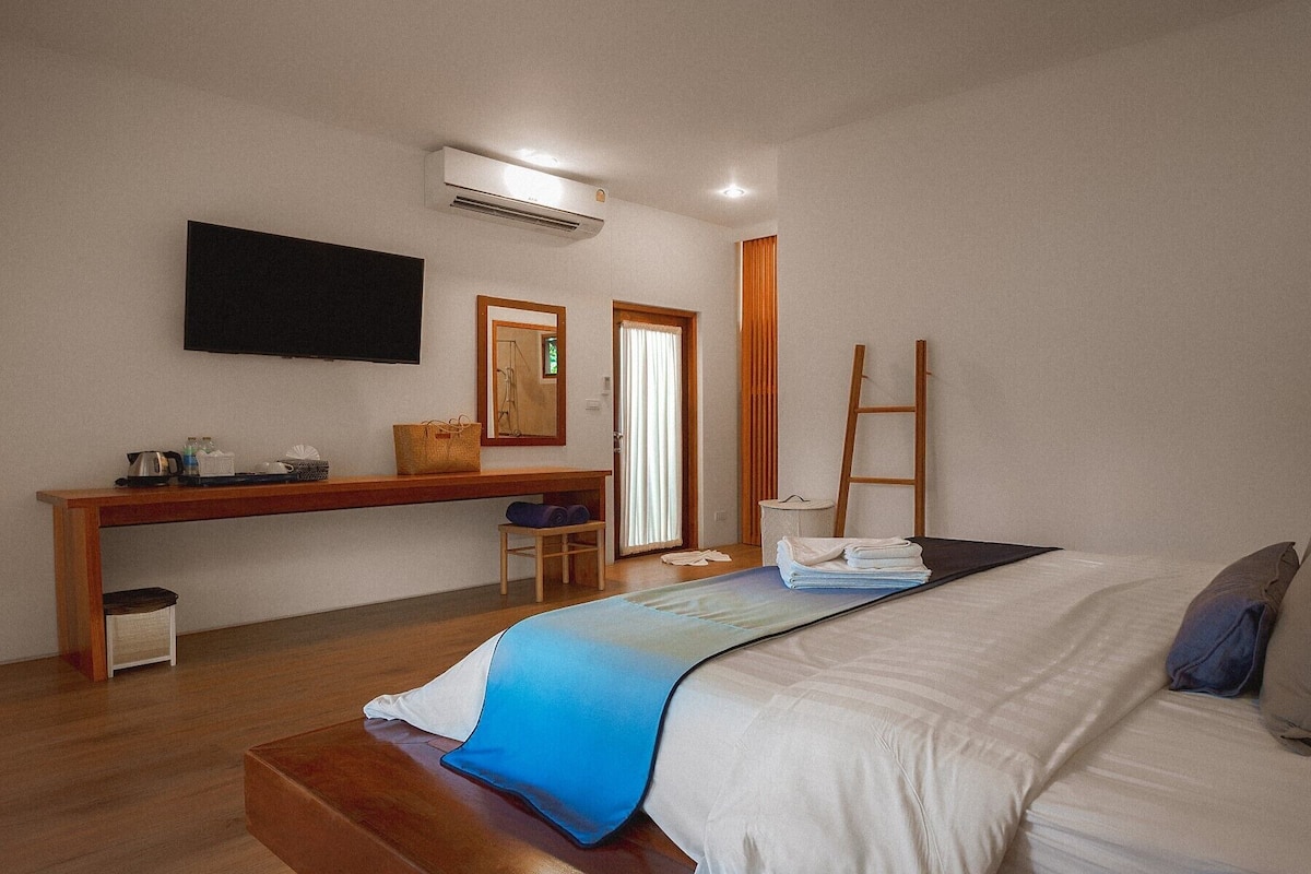 A hotel room with a bed, a desk with a chair, a television mounted on the wall, and a window with curtains.