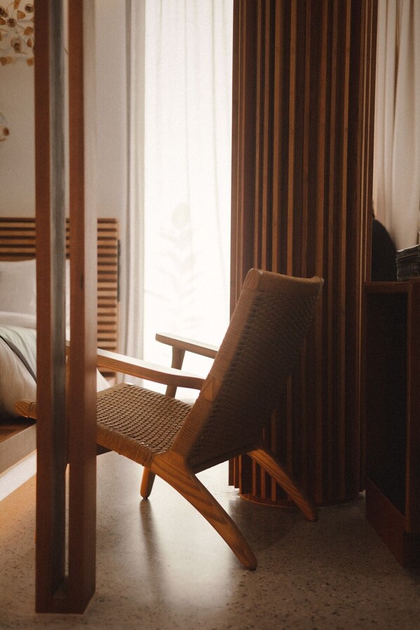 Una habitación de esquina con una silla de madera, una cama y una ventana con cortinas.