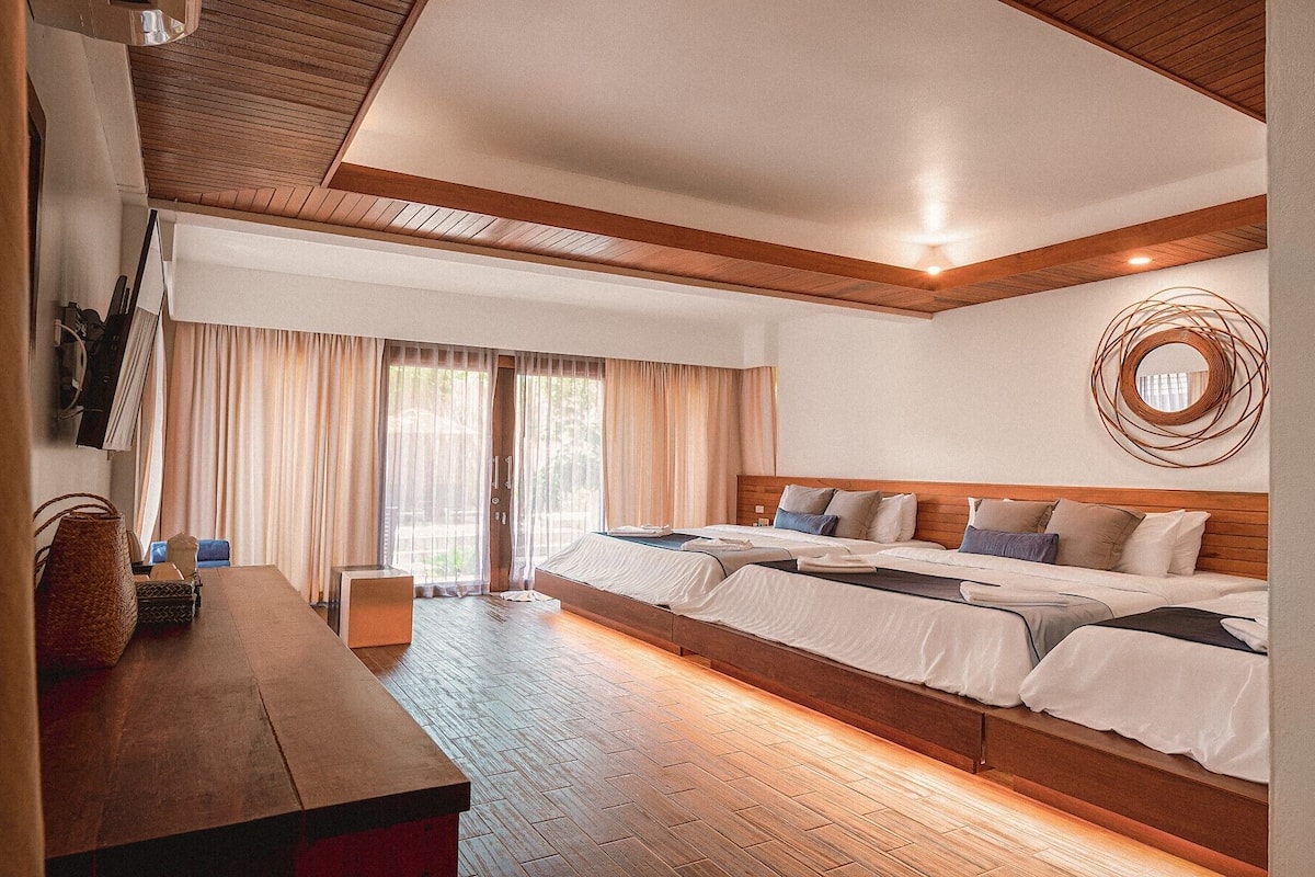 A hotel room with a large bed, a wooden bench, and a view of the outdoors.