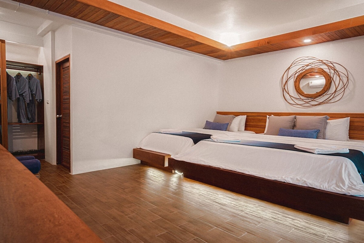 A bedroom with two beds, wooden headboards, a wooden ceiling, and a wall-mounted light fixture.