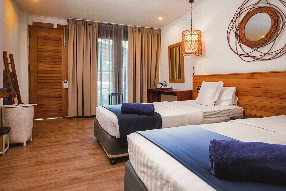 A hotel room with two beds, a wooden headboard, a mirror, a wicker lamp, and a wooden floor.