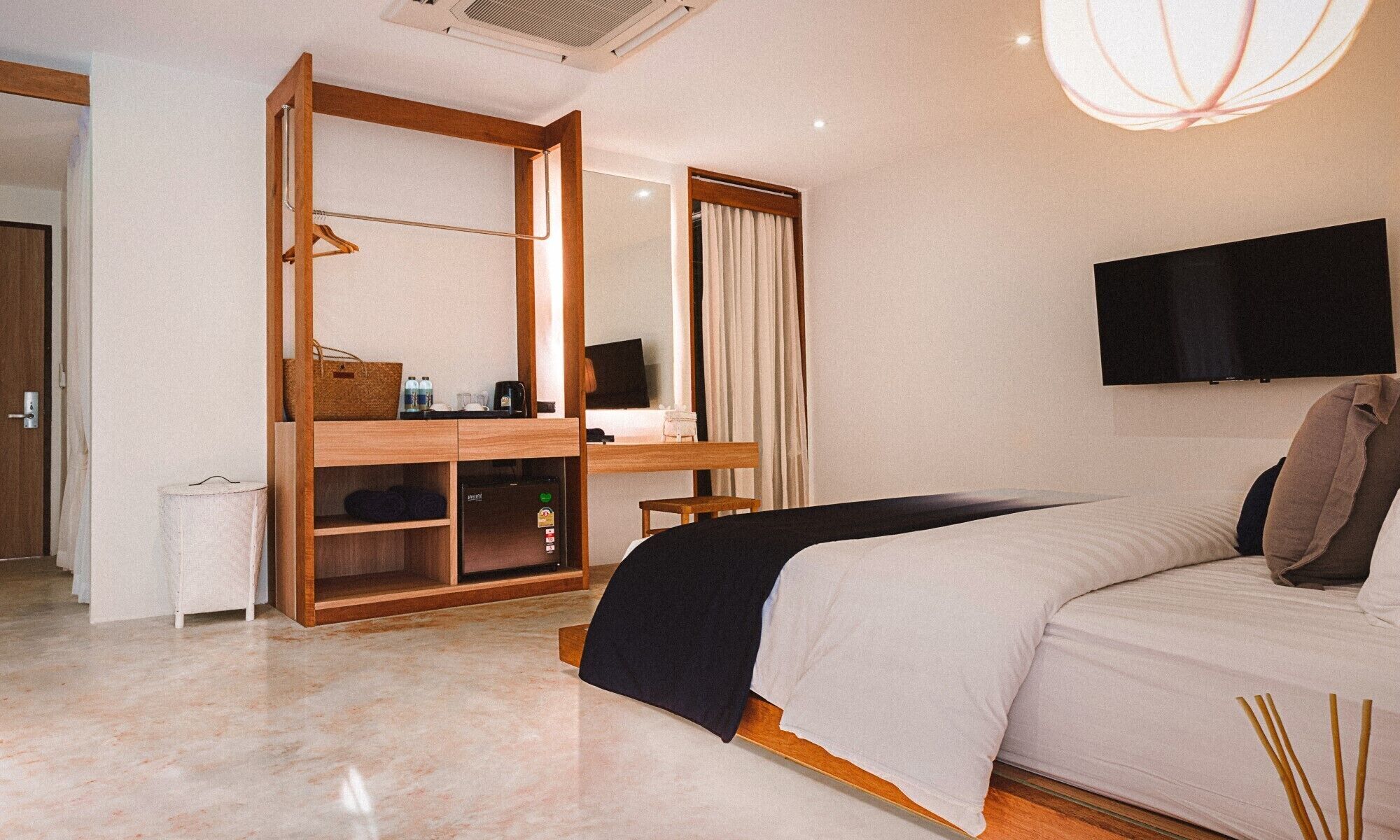 A hotel room with a bed, a desk with a chair, a television mounted on the wall, and a wardrobe.