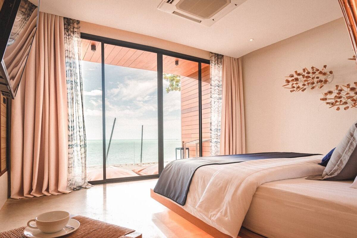 A bedroom with a bed, a view of the sea, and a dining area with a cup and saucer.