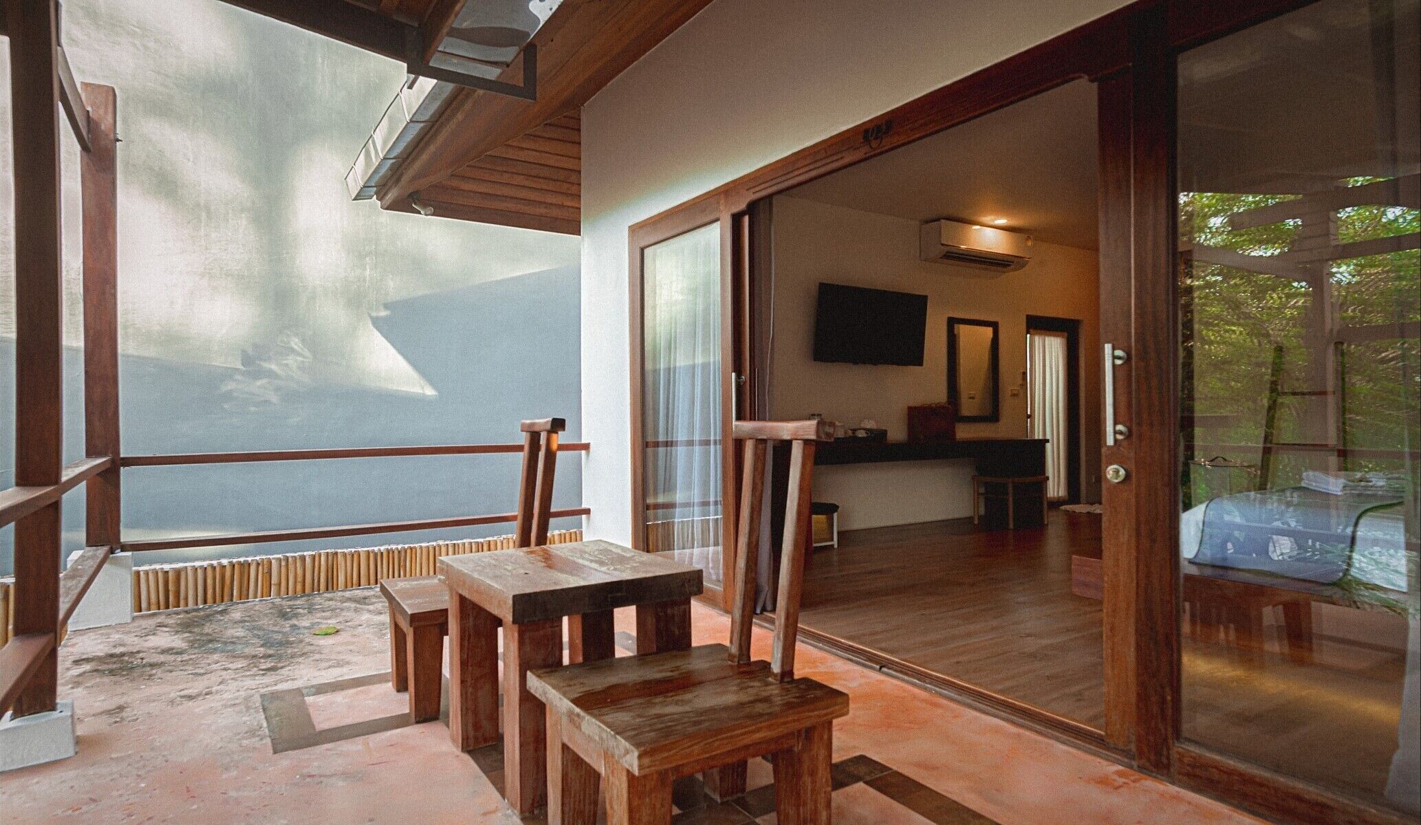 A wooden deck with a table and chairs, a sliding glass door leading to a room with a TV, and a view of the outdoors.