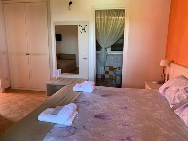 Un dormitorio con cama, armario, espejo y baño visible a través de una puerta abierta.