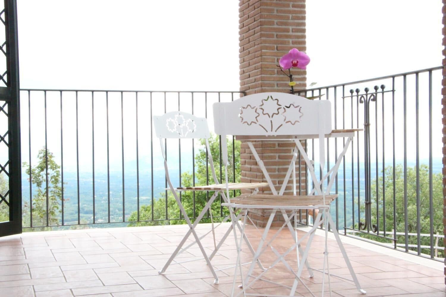 A balcony with a white metal chair and table, a brick pillar, and a view of the ocean.
