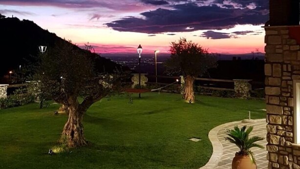 A landscaped garden with a stone pathway leading to a building, surrounded by trees and a view of a sunset.
