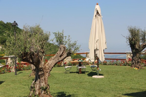 A garden with a table and chairs, a lamp post, and a large umbrella. - B&B I 4 Sentieri (Castel San Pietro Romano)