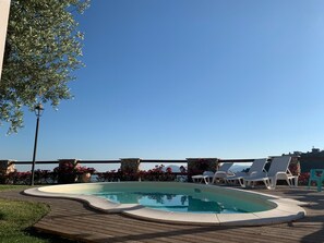 A pool area with a clear view of the ocean, surrounded by lounge chairs and a stone pillar. - B&B I 4 Sentieri (Castel San Pietro Romano)