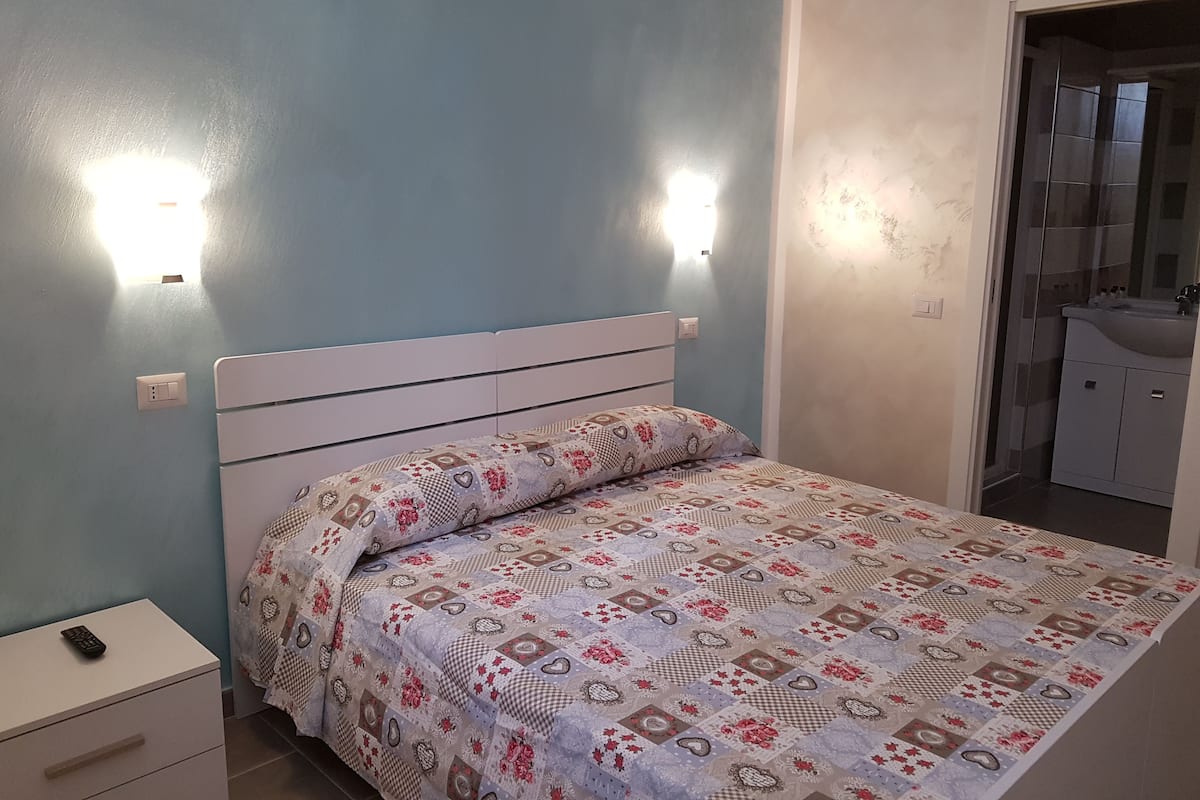 A bedroom with a bed, bedside table, and a bathroom visible through an open door.