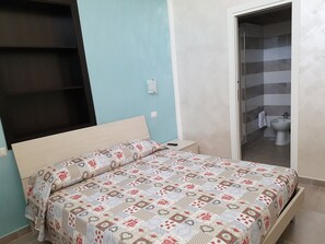 A bedroom with a bed, a bedside table, and a bathroom visible through an open door.