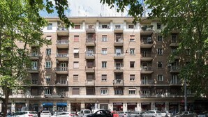 Ein mehrstöckiges Wohnhaus mit Balkonen, einem Parkplatz davor und Geschäften im Erdgeschoss.